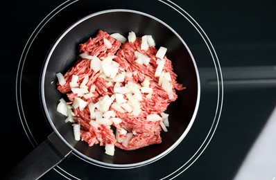 Photo of Frying pan with raw minced meat and chopped onion on induction stove, top view