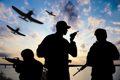 Silhouettes of soldiers in uniform with assault rifles and military airplanes patrolling outdoors