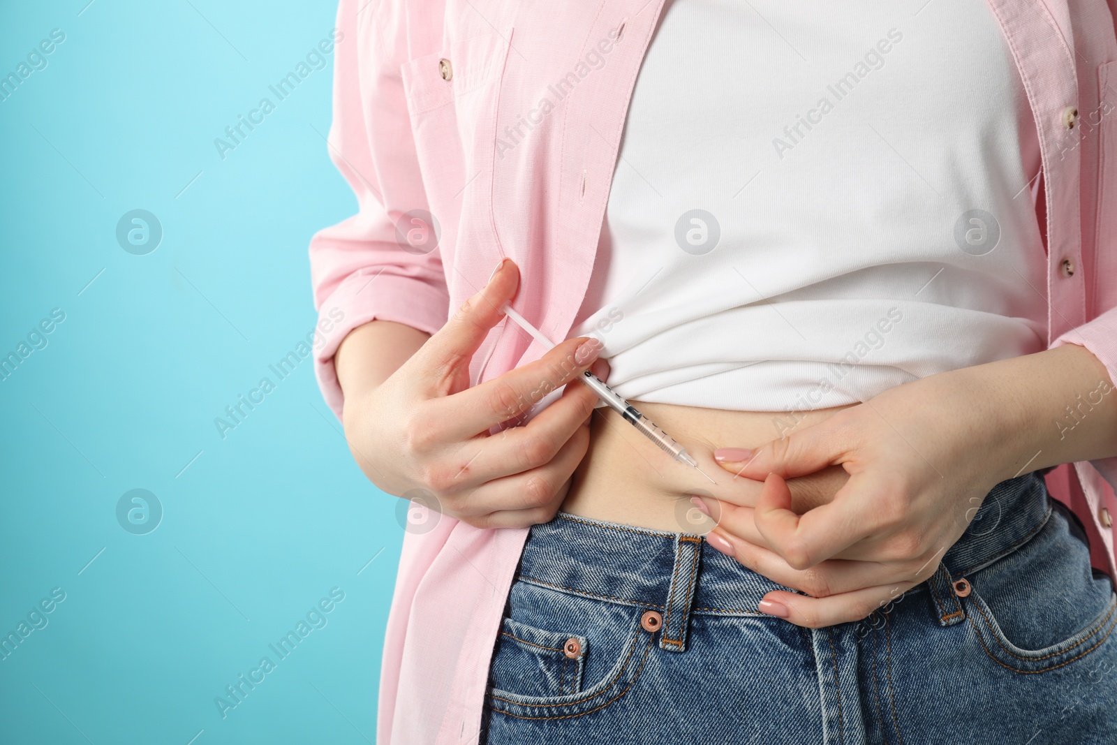 Photo of Diabetes. Woman making insulin injection into her belly on light blue background, closeup