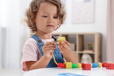 Photo of Motor skills development. Little girl playing with wooden pieces and string for threading activity at table indoors