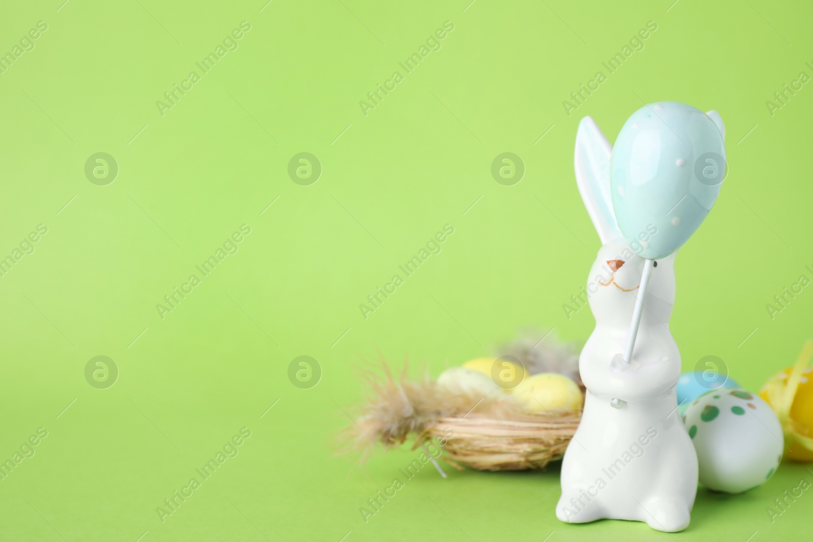 Photo of Easter bunny figure, nest and dyed eggs on green background. Space for text