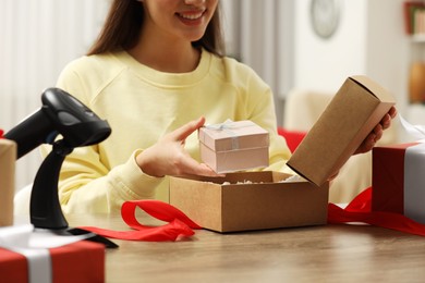 Photo of Woman putting Christmas gift box into parcel at wooden table in post office, closeup