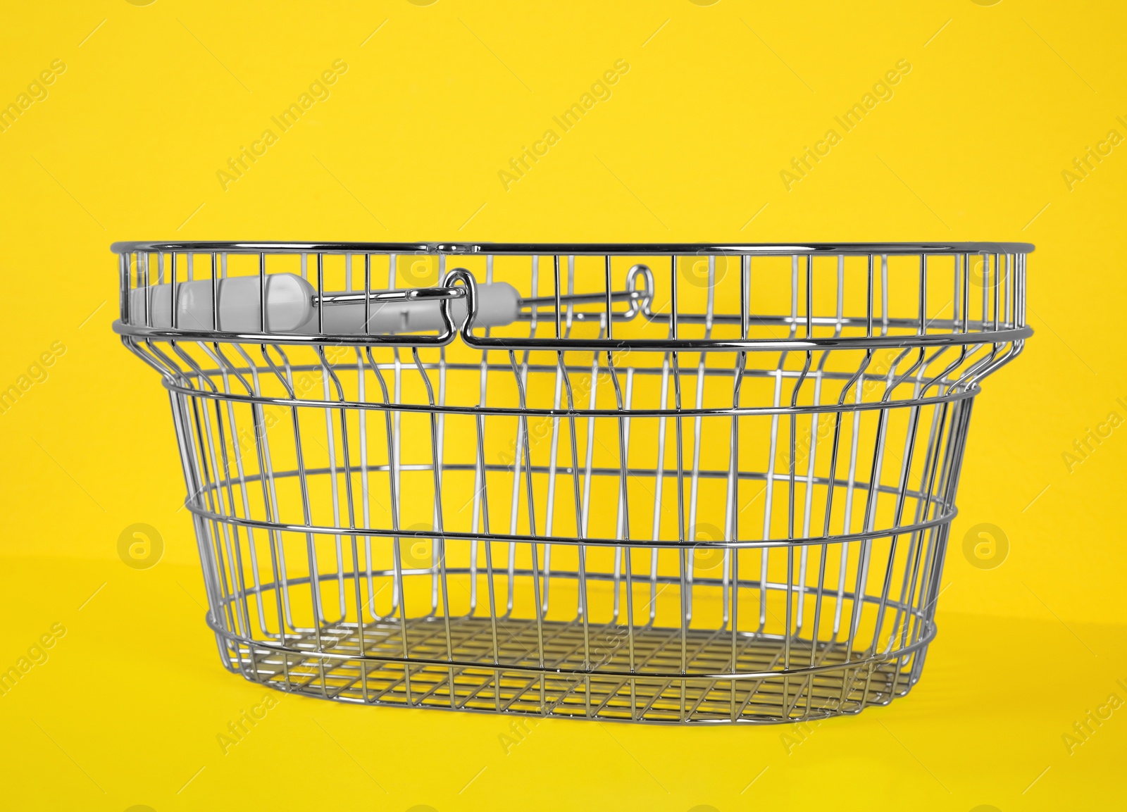 Photo of Empty metal shopping basket on yellow background