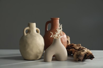 Clay flagons, vase, dried flowers and wooden snag on white marble table