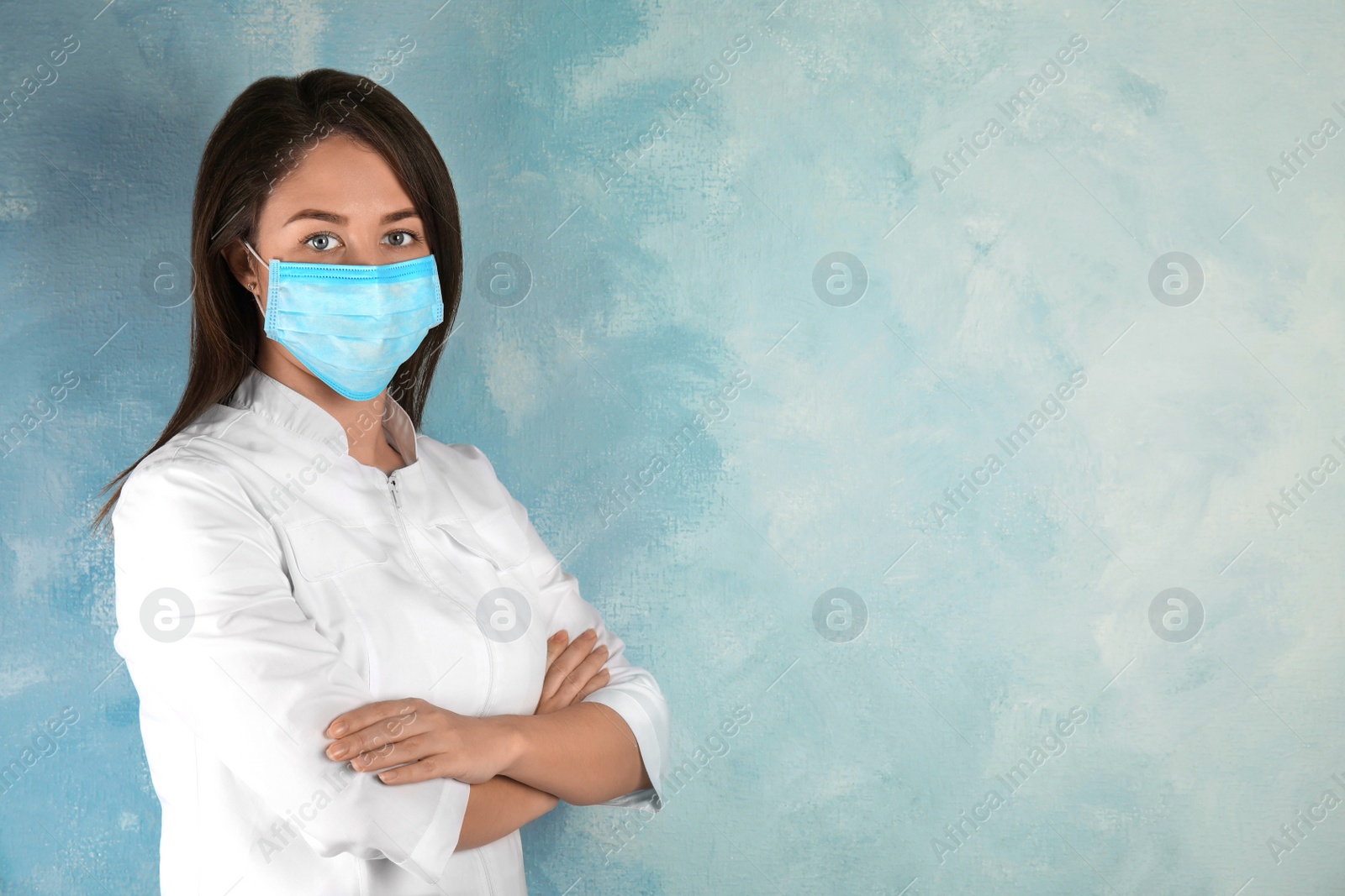 Photo of Doctor with disposable mask on face against light blue background. Space for text