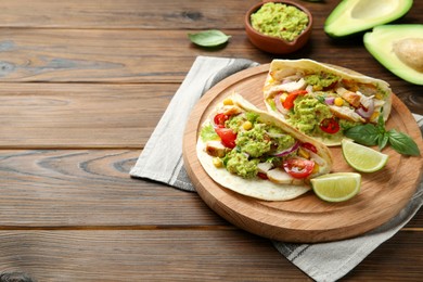 Delicious tacos with guacamole, meat and vegetables served with lime on wooden table. Space for text