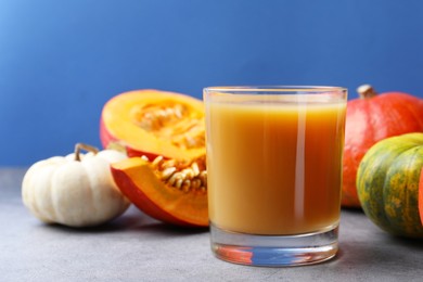 Photo of Tasty pumpkin juice in glass and different pumpkins on light grey table against blue background. Space for text