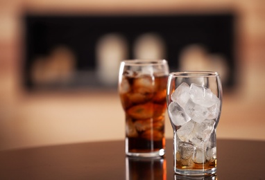 Photo of Glasses with cola and ice cubes on table against blurred background. Space for text