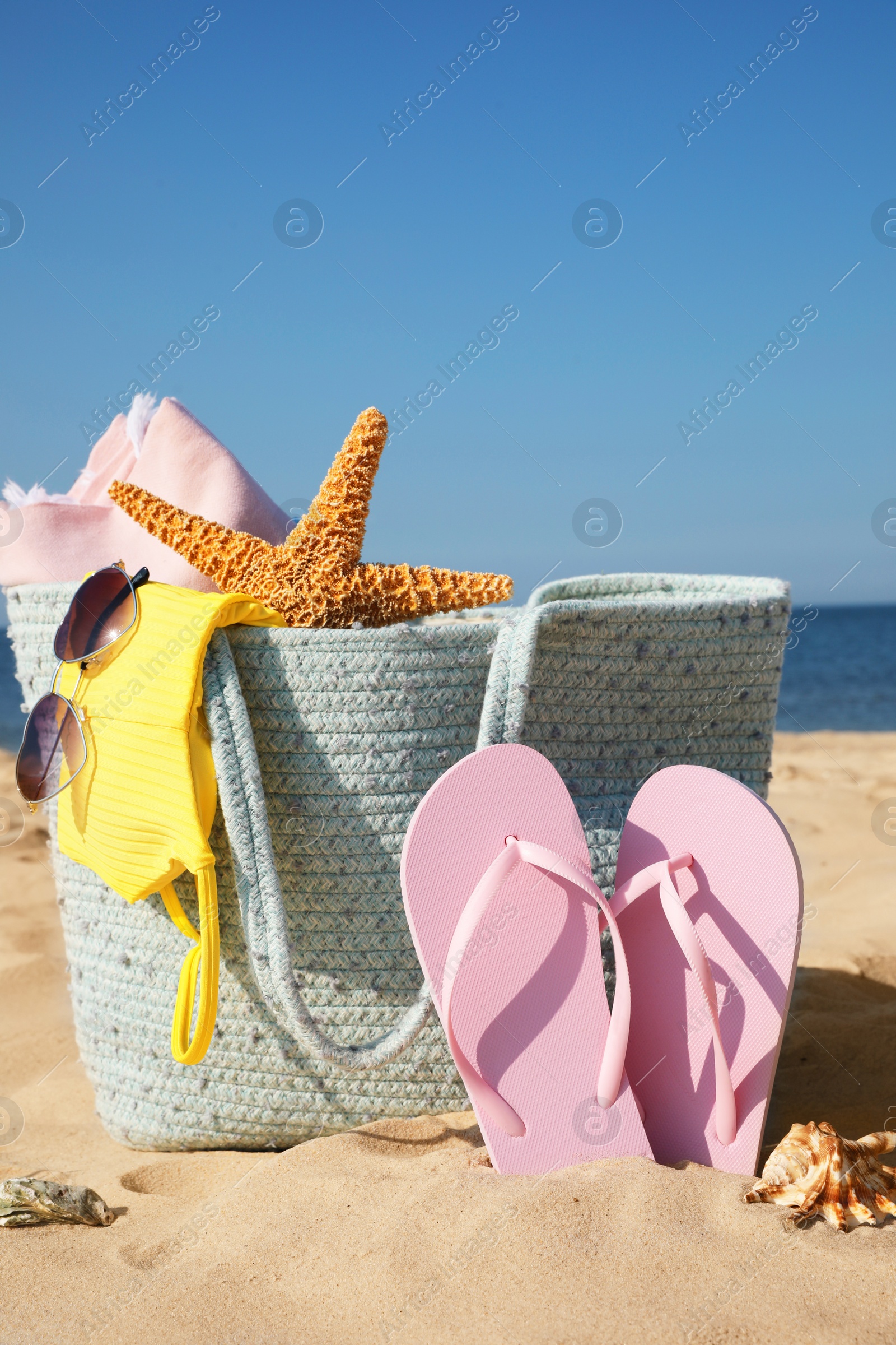 Photo of Bag with beach accessories and flip flops on sand near sea