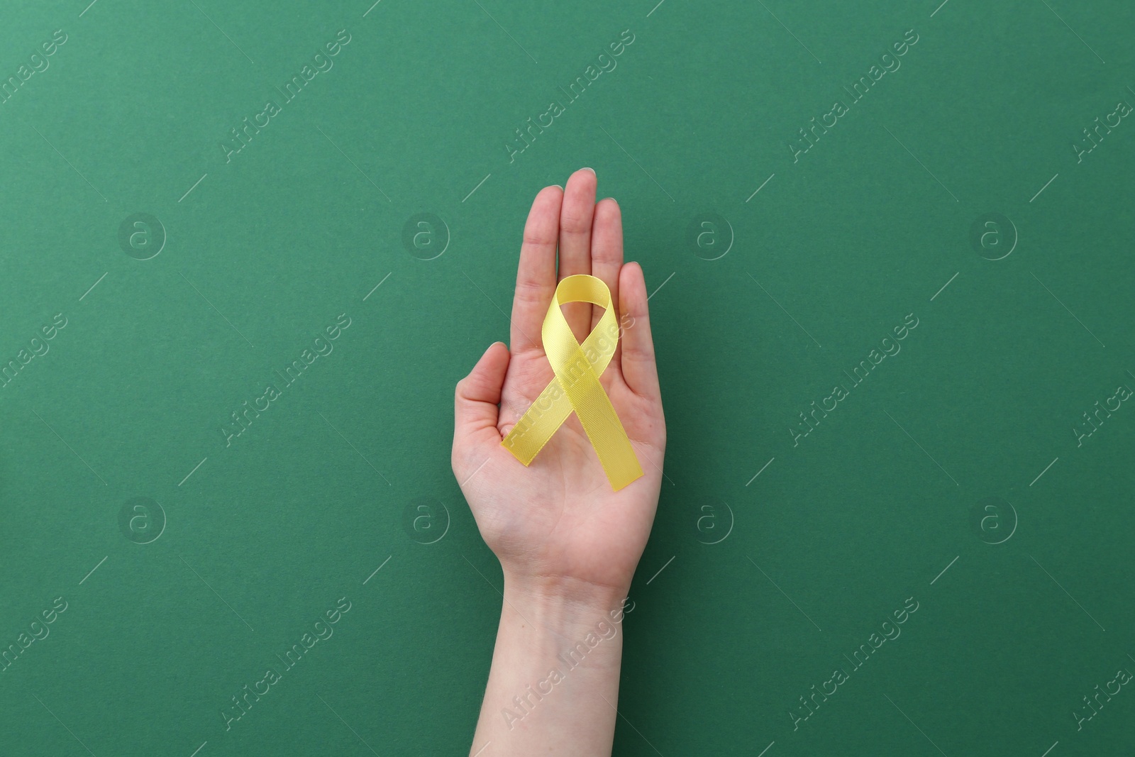 Photo of Woman with yellow awareness ribbon on green background, top view