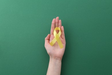 Woman with yellow awareness ribbon on green background, top view