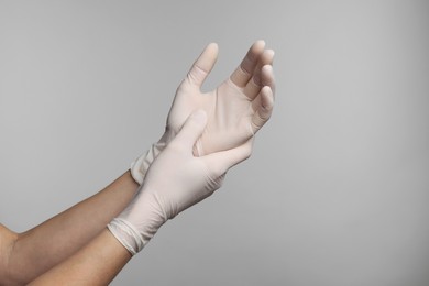 Doctor wearing white medical gloves on grey background, closeup