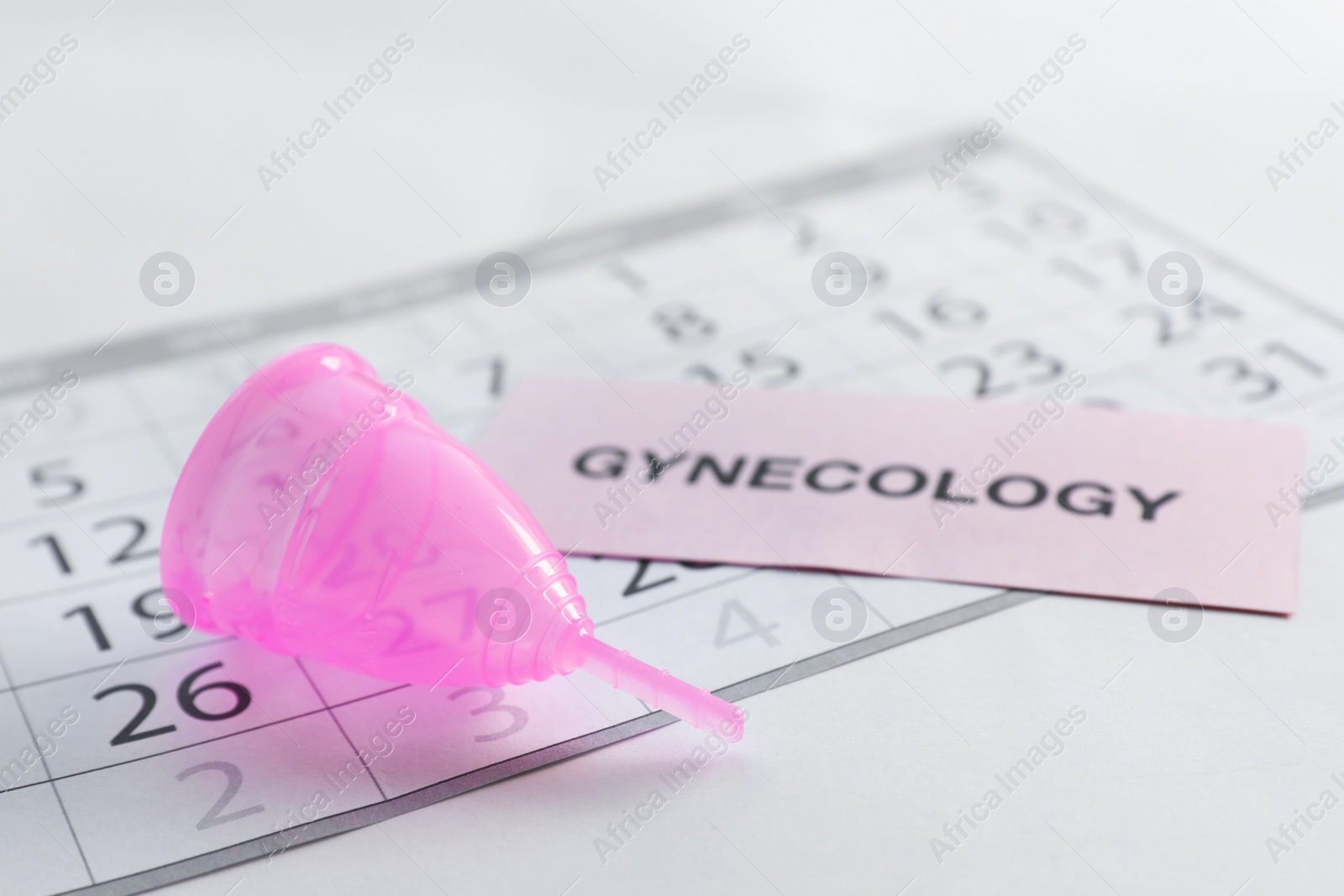 Photo of Menstrual cup, calendar and card with word GYNECOLOGY on light background