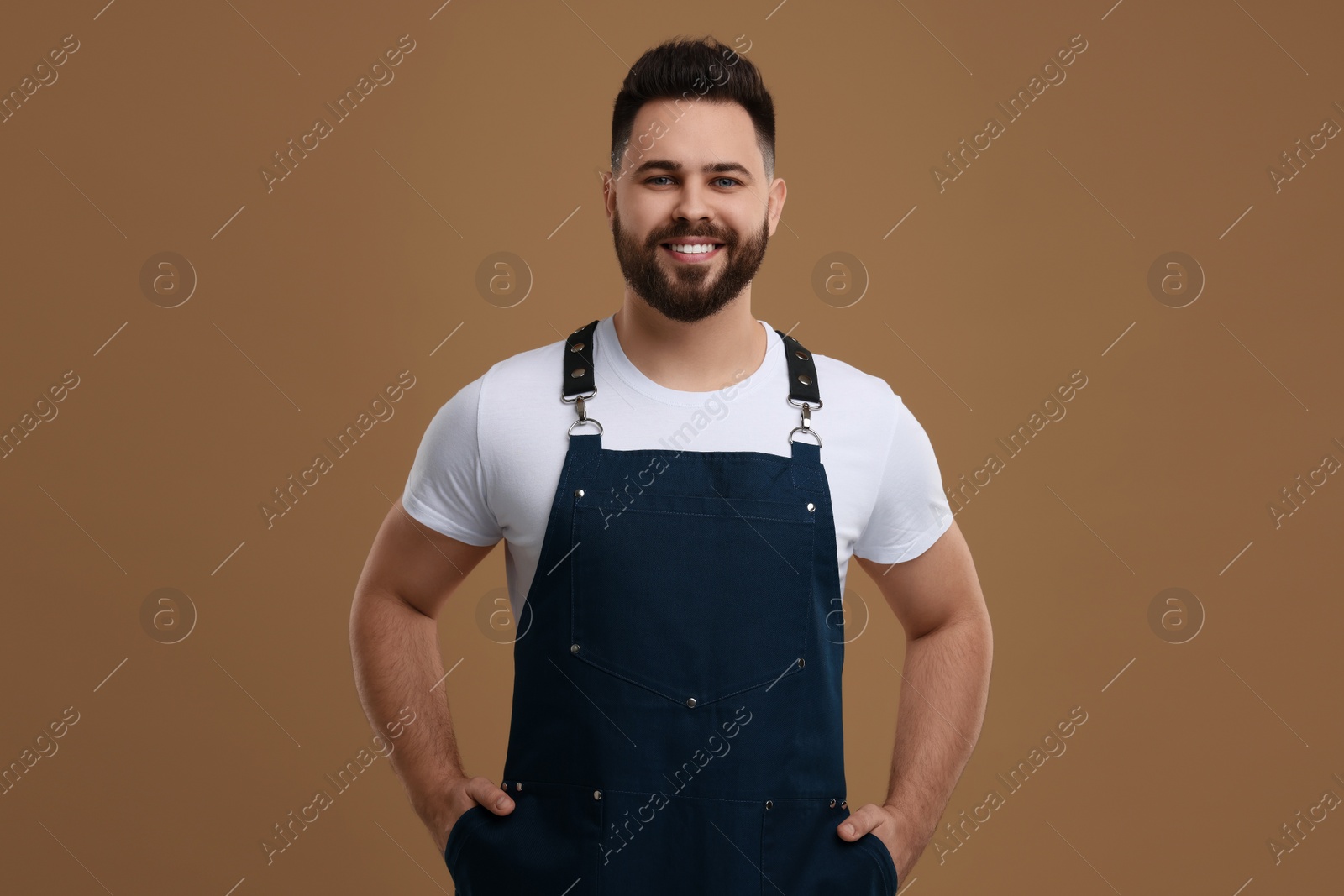 Photo of Smiling man in kitchen apron on brown background. Mockup for design