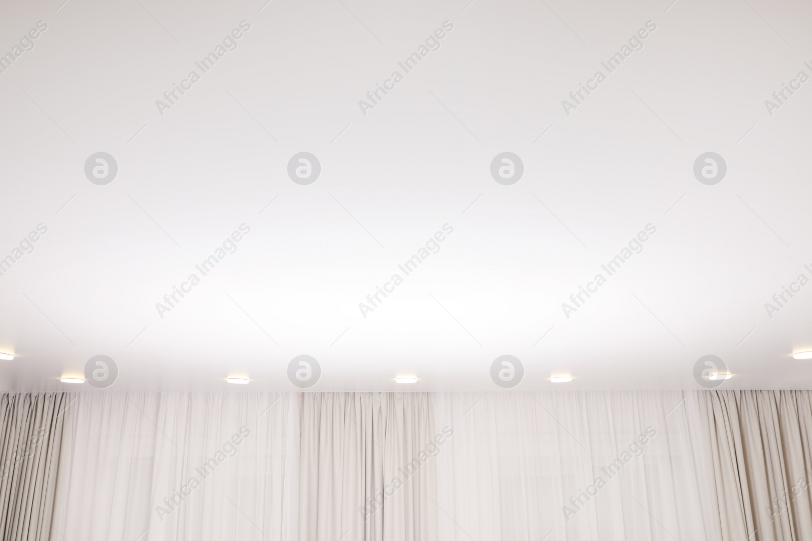 Photo of White stretch ceiling with spot lights in room, low angle view