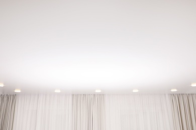 Photo of White stretch ceiling with spot lights in room, low angle view