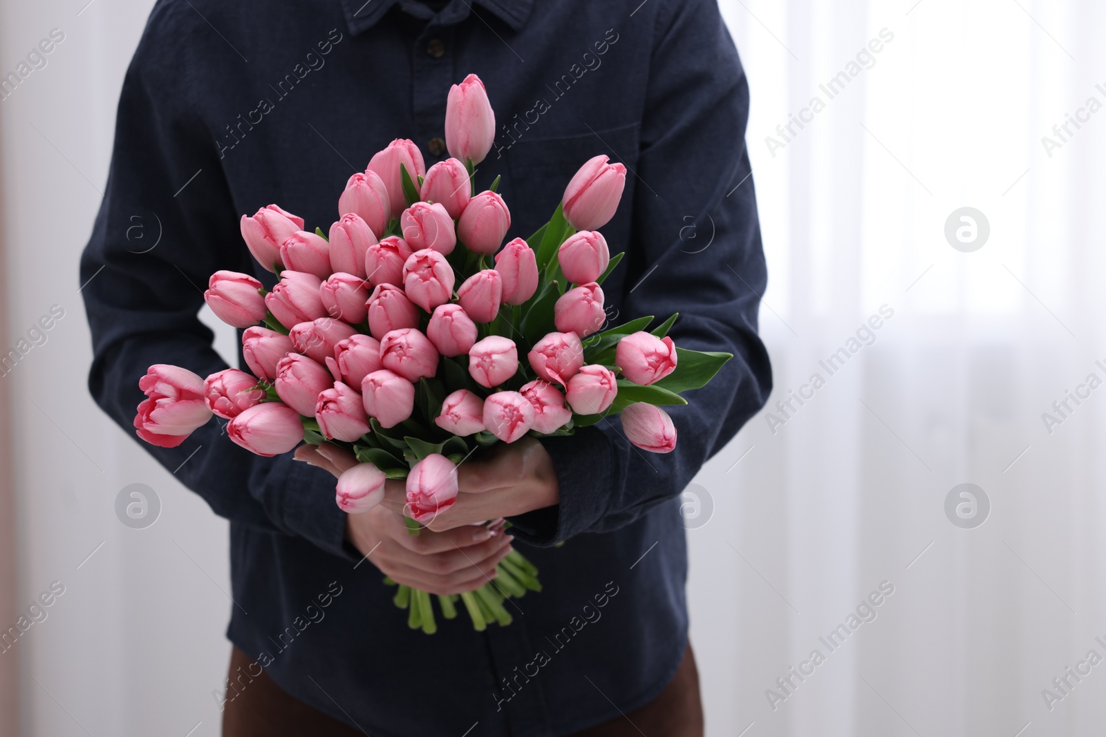 Photo of Woman holding bouquet of pink tulips indoors, closeup. Space for text