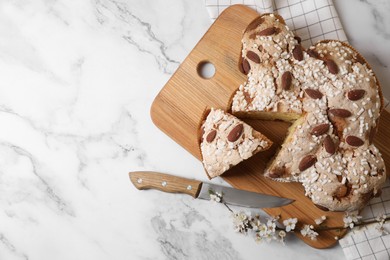 Delicious Italian Easter dove cake (traditional Colomba di Pasqua), knife and branch with beautiful flowers on white marble table, top view. Space for text