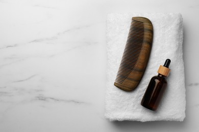 Photo of Wooden hair comb, bottle of essential oil and terry towel on white marble table, top view. Space for text