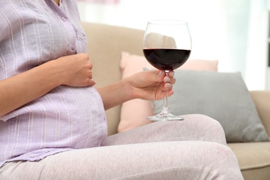 Photo of Future mother with glass of wine at home, closeup. Alcohol abuse during pregnancy