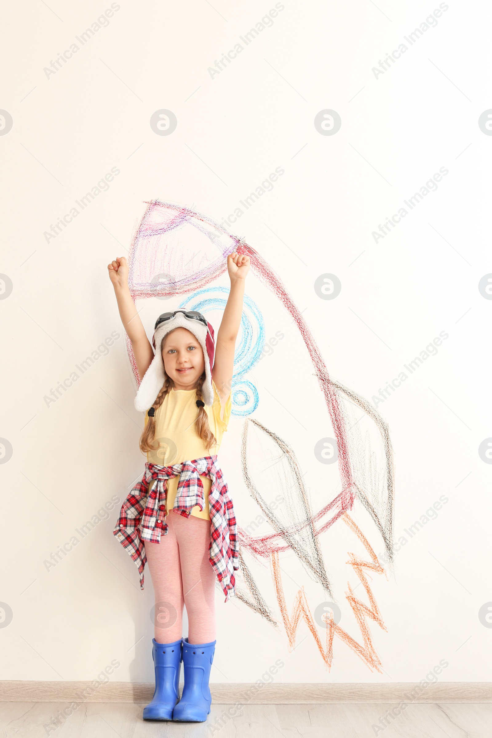 Photo of Adorable little child playing astronaut near wall with drawing of spaceship indoors