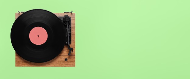 Modern turntable with vinyl record on green background, top view