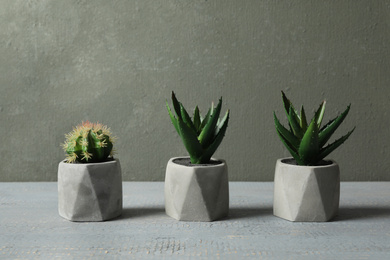 Photo of Artificial plants in ceramic flower pots on grey wooden table