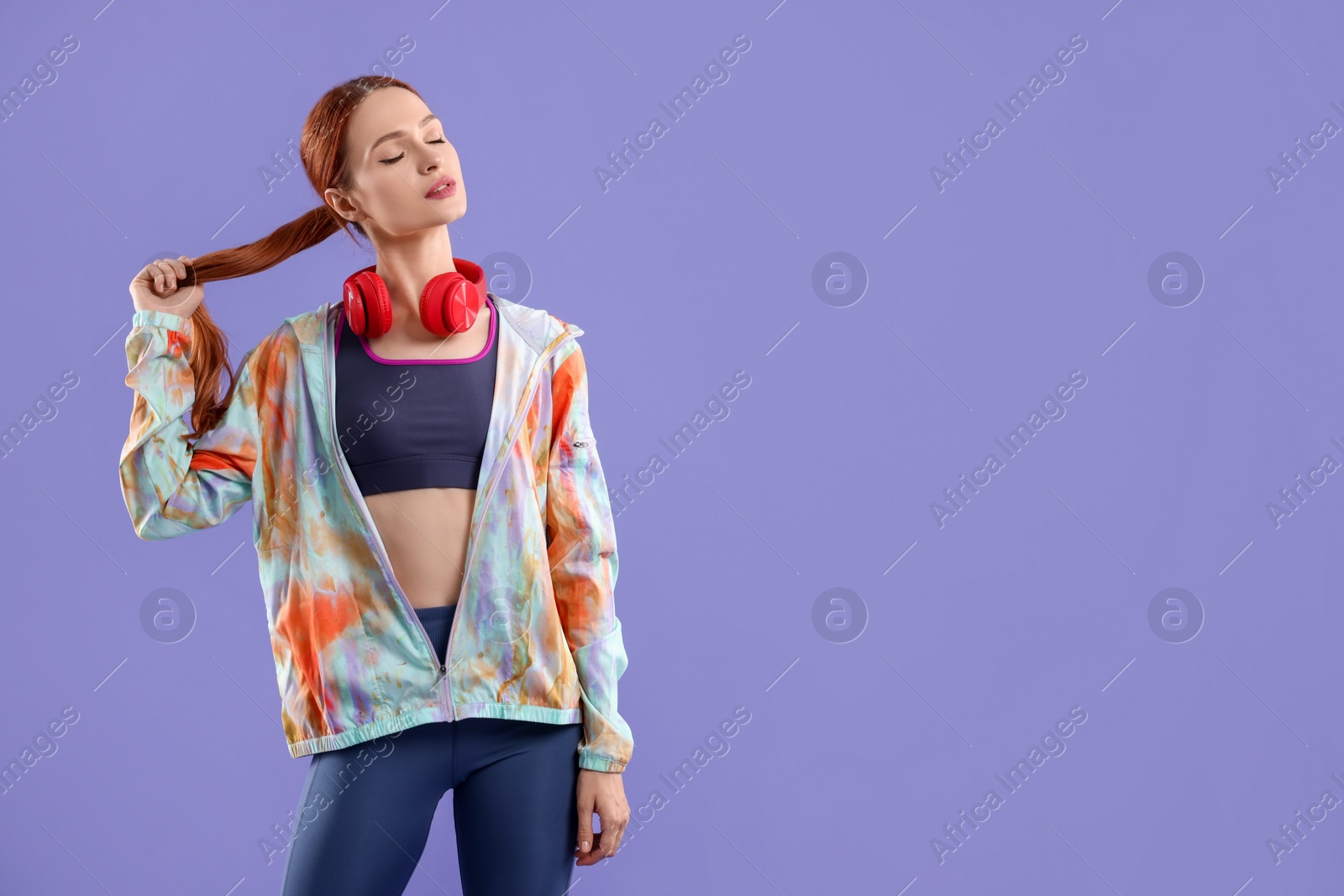 Photo of Young woman in sportswear and headphones on violet background, space for text