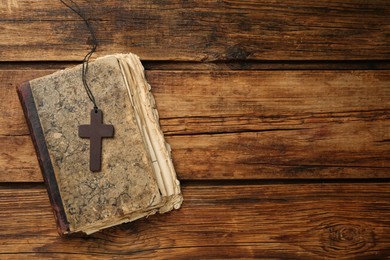 Photo of Christian cross and Bible on wooden table, top view. Space for text