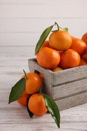 Photo of Delicious tangerines with leaves on light wooden table