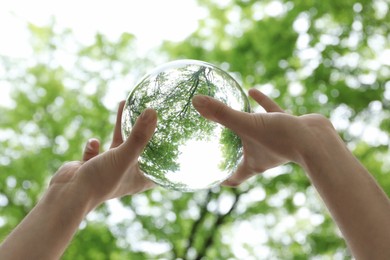 Overturned reflection of beautiful green trees outdoors, low angle view. Man holding crystal ball in park, closeup