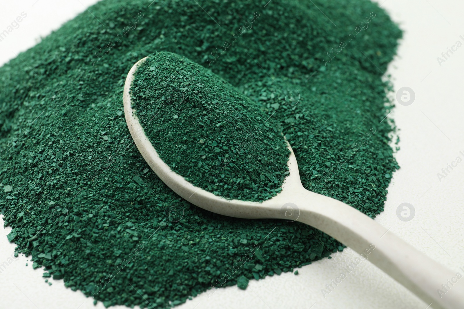 Photo of Spoon with spirulina algae powder on white background, closeup