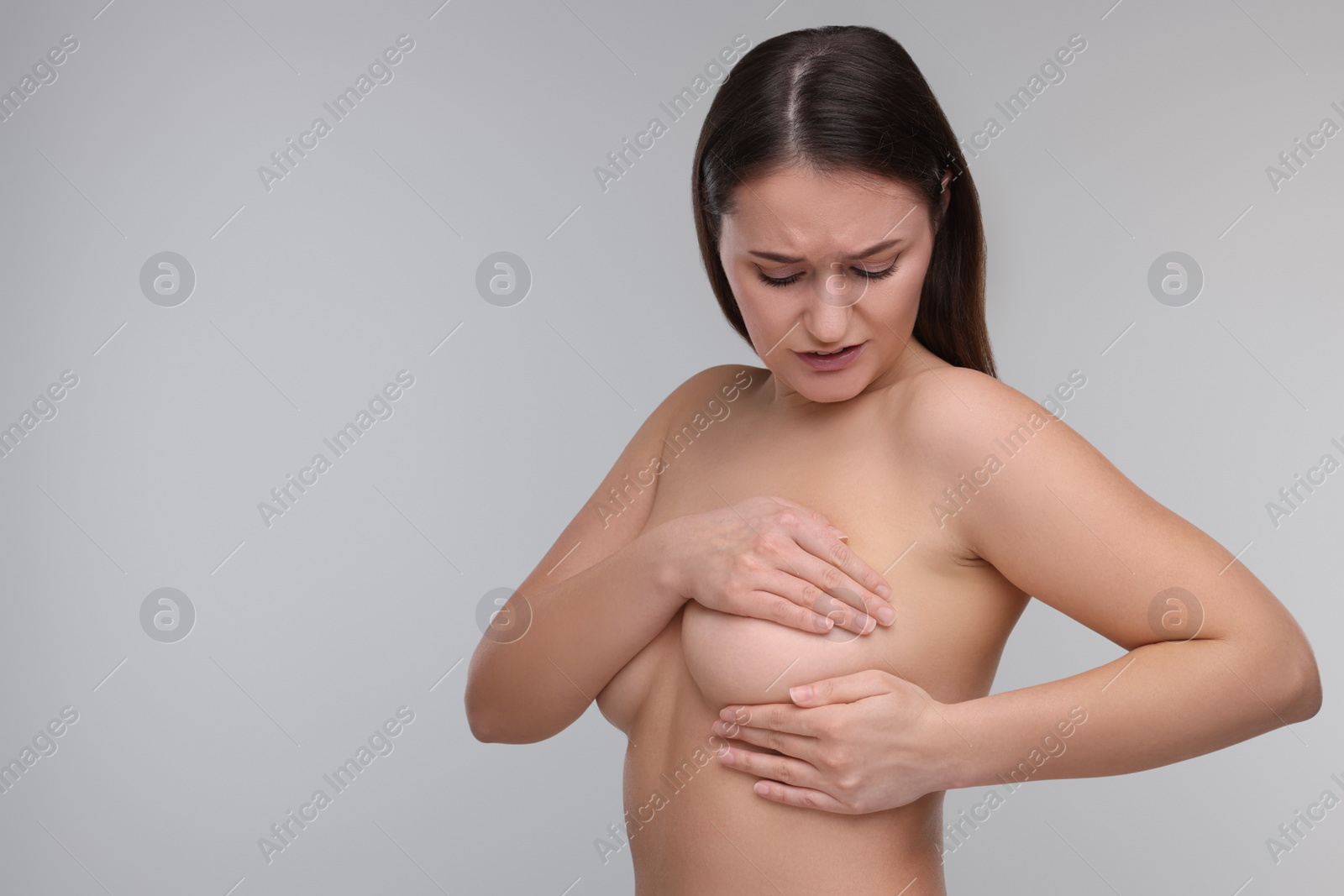 Photo of Mammology. Naked woman doing breast self-examination on light grey background, space for text