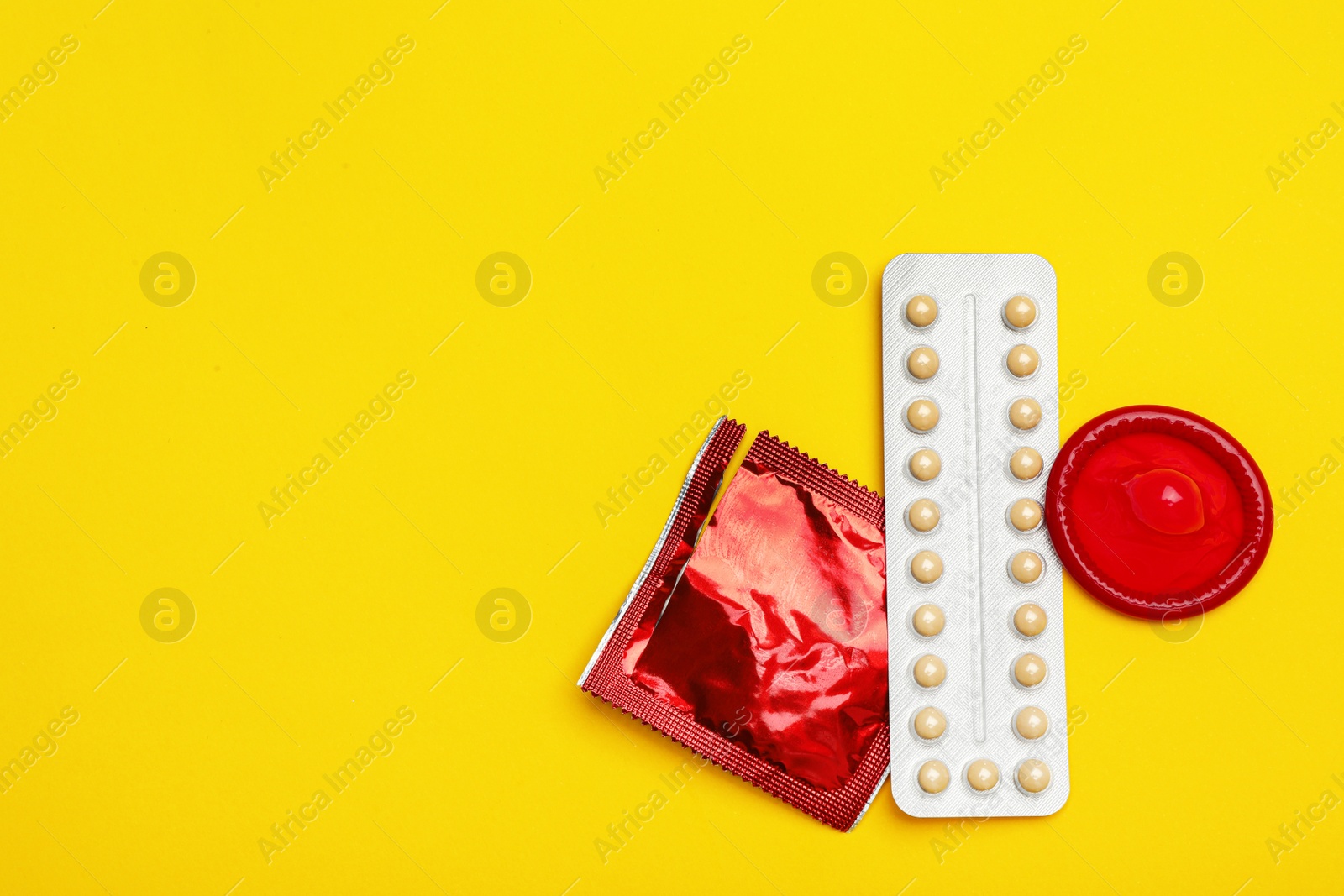 Photo of Condoms and birth control pills on yellow background, flat lay with space for text. Safe sex concept