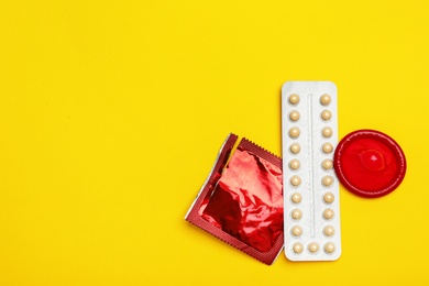 Condoms and birth control pills on yellow background, flat lay with space for text. Safe sex concept