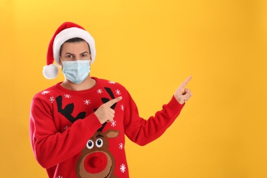 Photo of Man wearing Santa hat and medical mask on yellow background, space for text