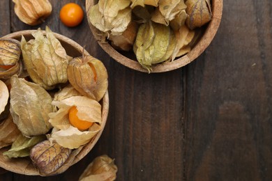 Photo of Ripe physalis fruits with calyxes in bowls on wooden table, flat lay. Space for text