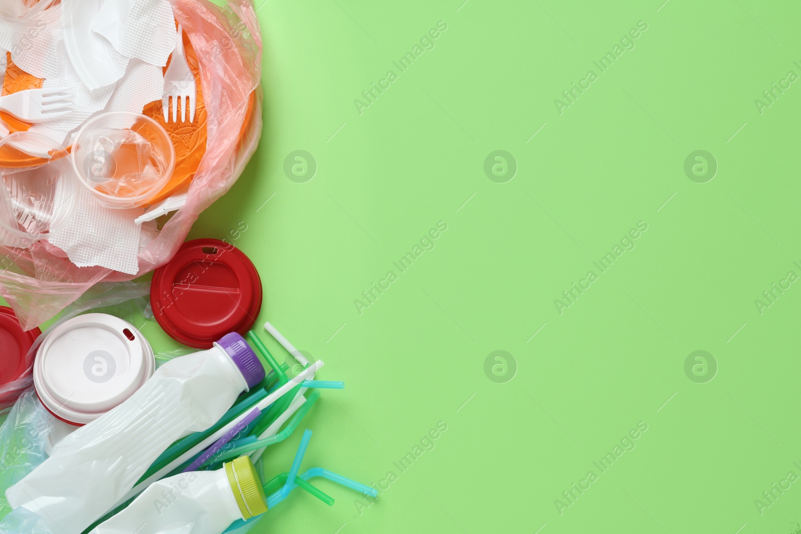 Photo of Pile of different plastic items on green background, flat lay. Space for text