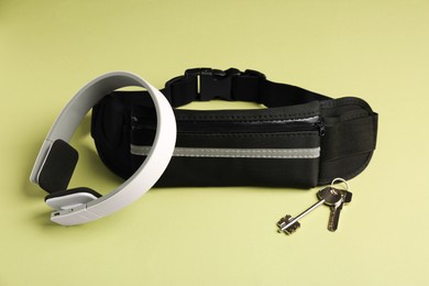 Photo of Stylish black waist bag, headphones and keys on green background