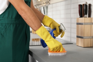 Photo of Male janitor cleaning kitchen counter with brush, closeup