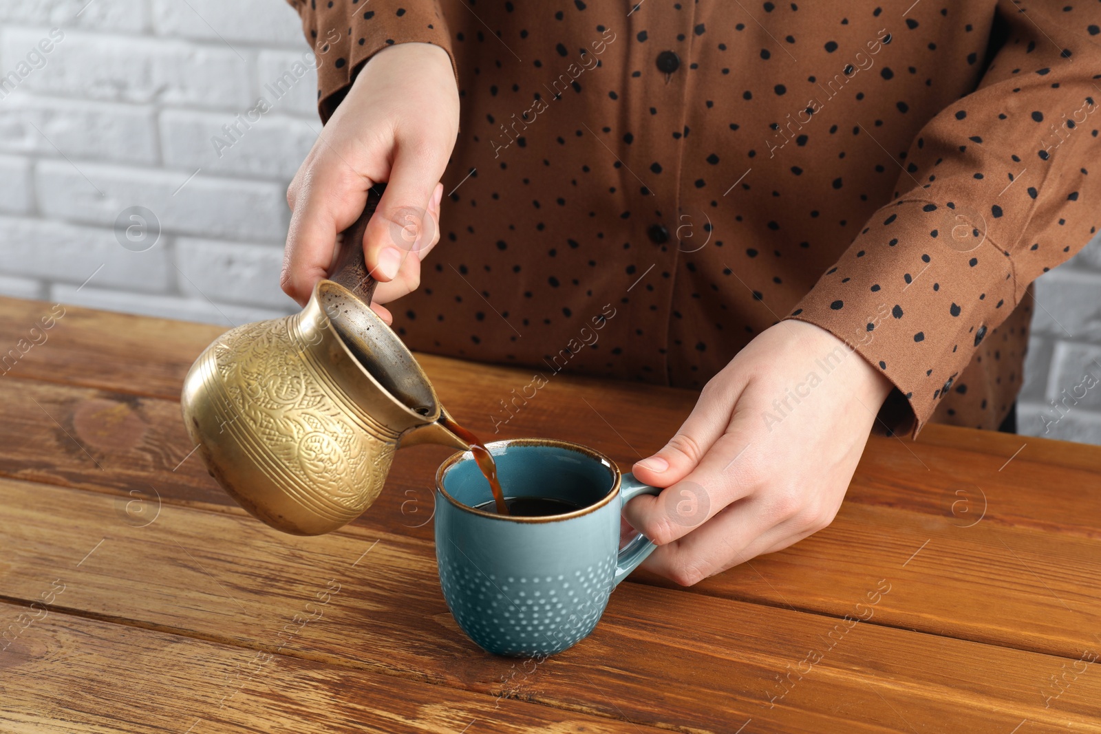 Photo of Turkish coffee. Woman pouring brewed beverage from cezve into cup at wooden table, closeup