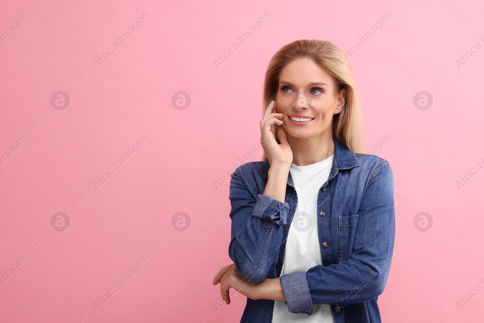 Photo of Portrait of smiling middle aged woman with blonde hair on pink background. Space for text