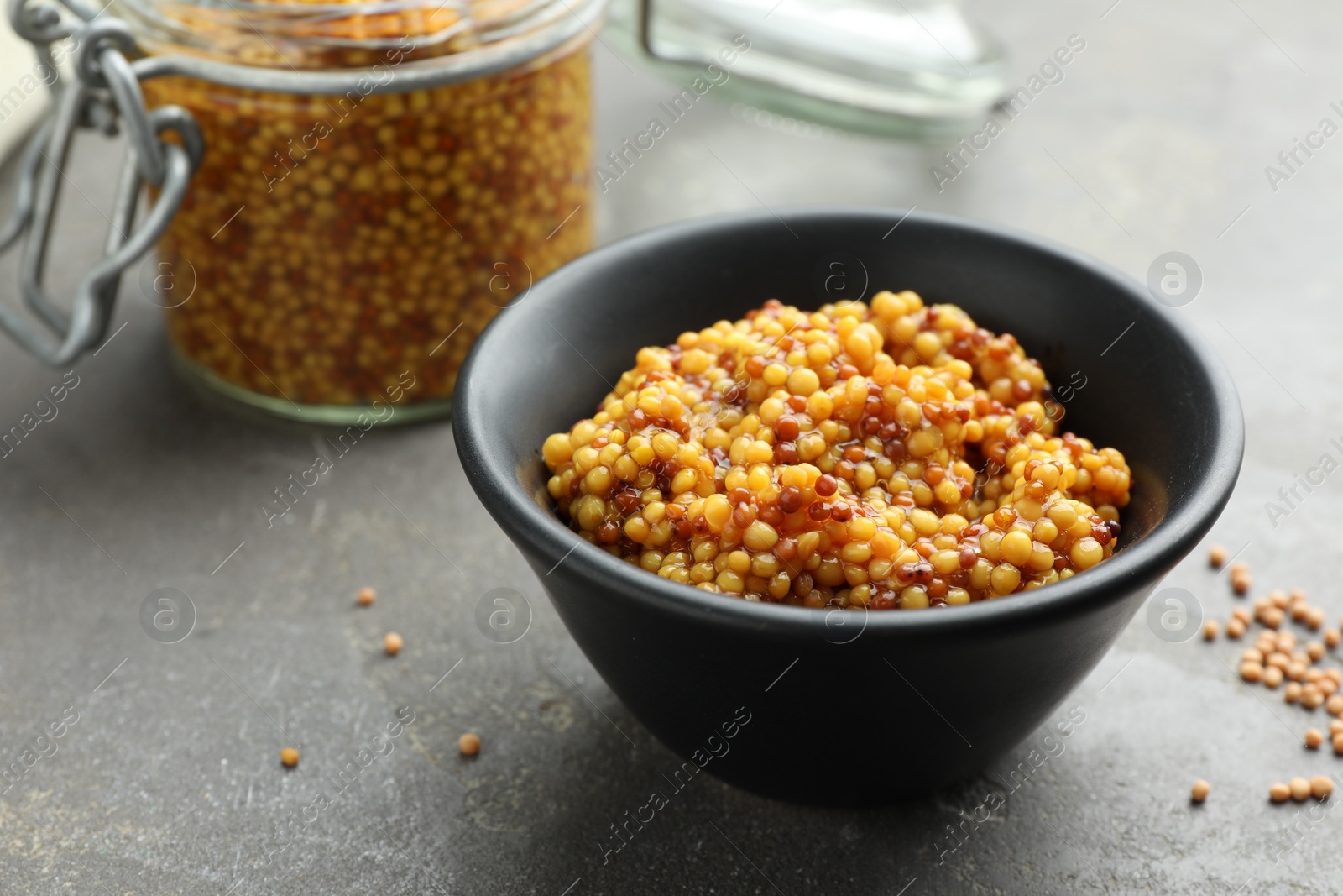 Photo of Whole grain mustard in bowl and dry seeds on grey table. Space for text