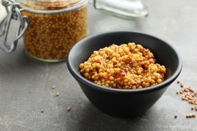 Whole grain mustard in bowl and dry seeds on grey table. Space for text