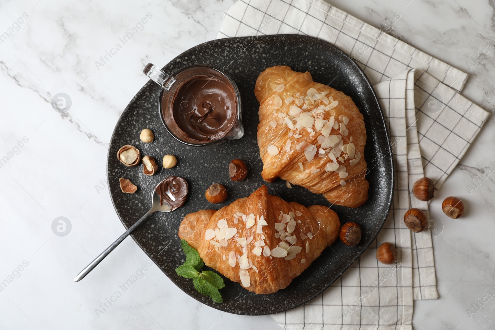 Photo of Delicious croissants with chocolate, nuts and spoon on white marble table, flat lay