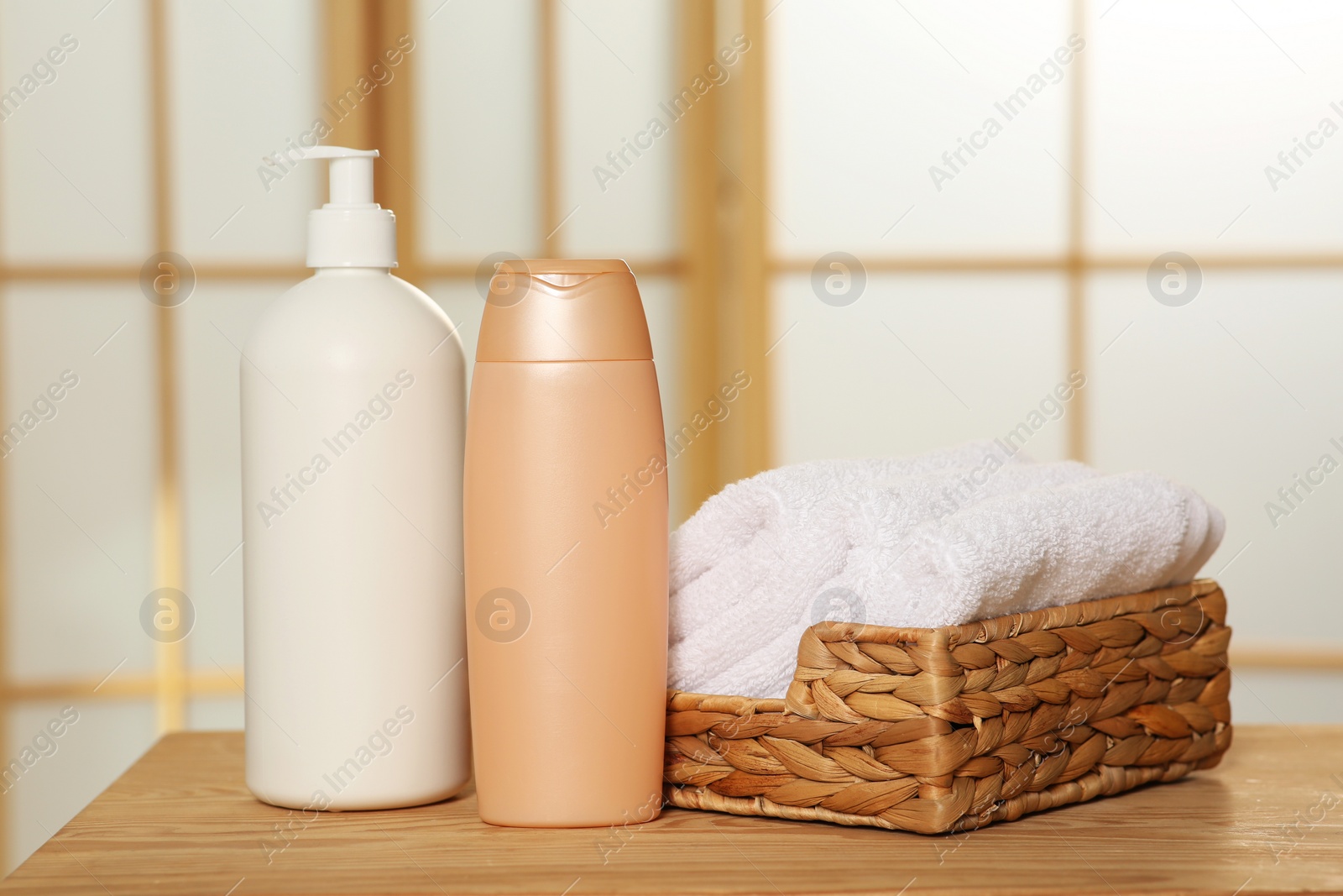 Photo of Soft folded terry towels in wicker basket and cosmetic bottles on wooden table indoors