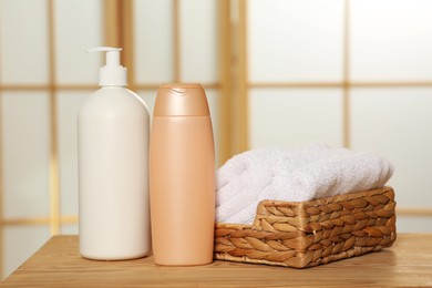 Photo of Soft folded terry towels in wicker basket and cosmetic bottles on wooden table indoors