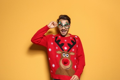 Young man in Christmas sweater with party glasses on color background