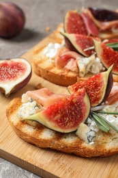 Photo of Bruschettas with cheese, prosciutto and figs served on wooden board, closeup