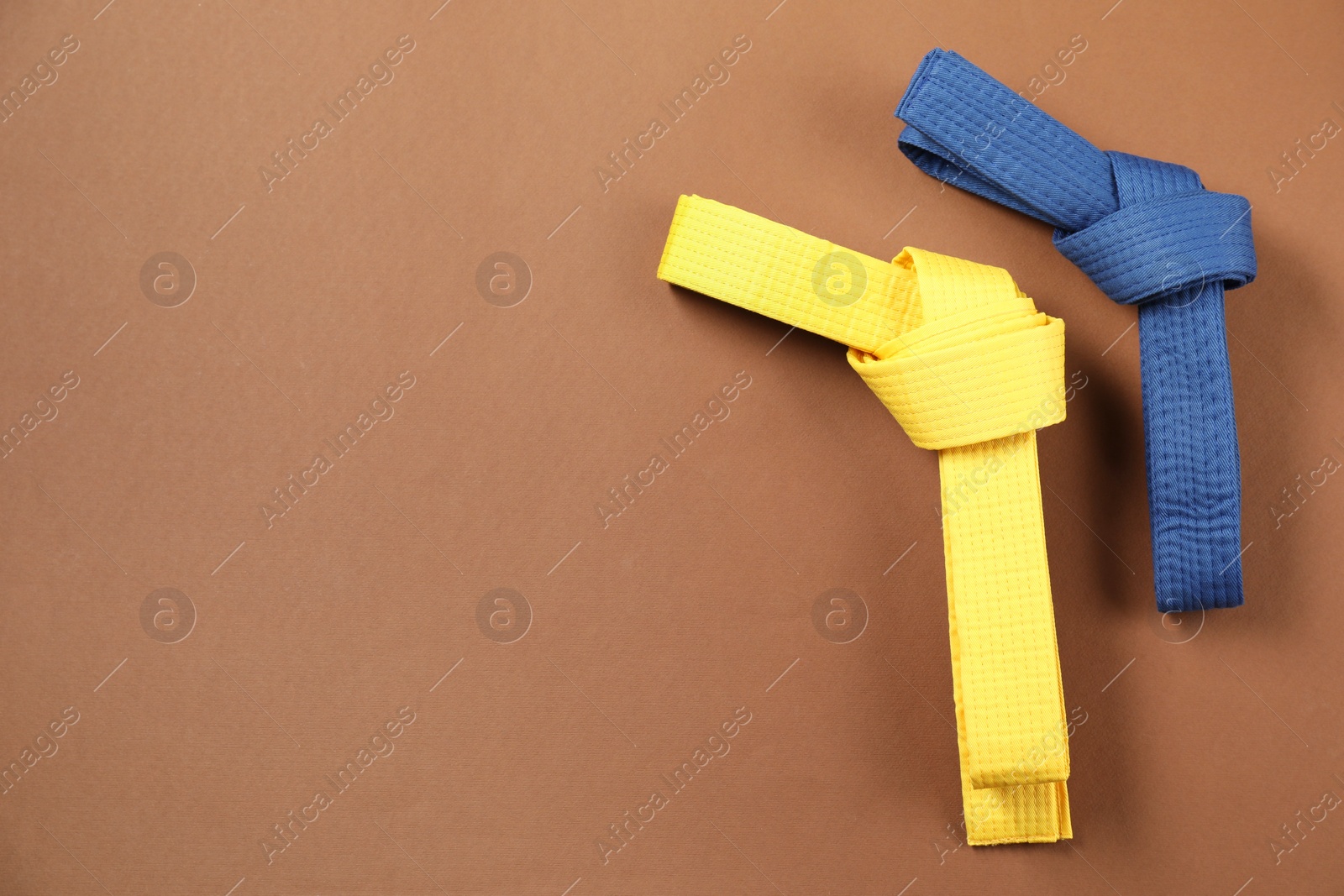 Photo of Yellow and blue karate belts on brown background, flat lay. Space for text